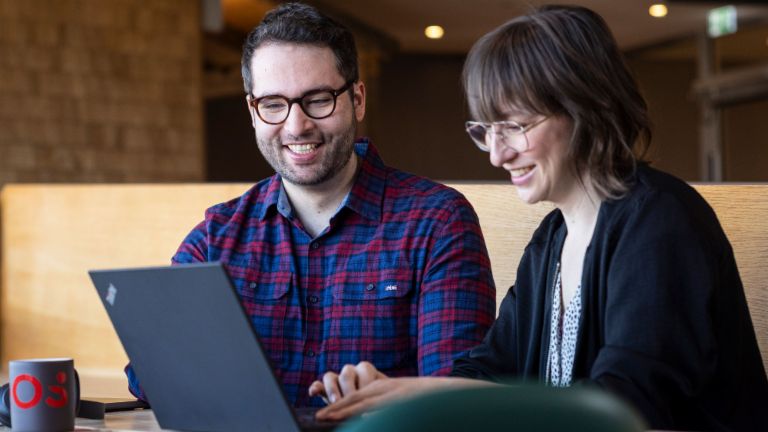 Two EOS employees look at a laptop together while engrossed in a conversation.