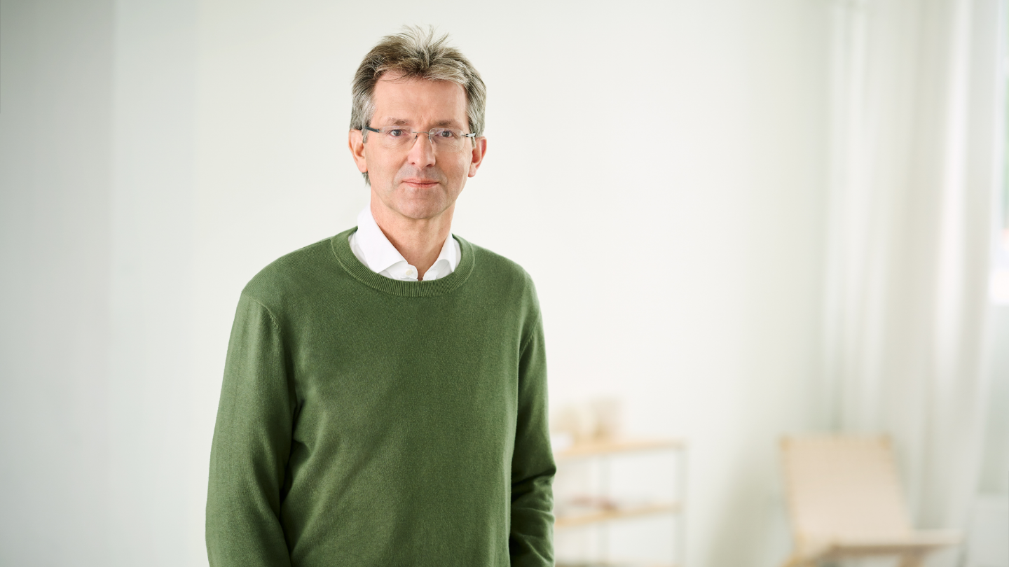 Justus Hecking-Veltman, CFO, mit einem wald-grünen Pullover und weißem Hemd, steht in einem hellen Raum.