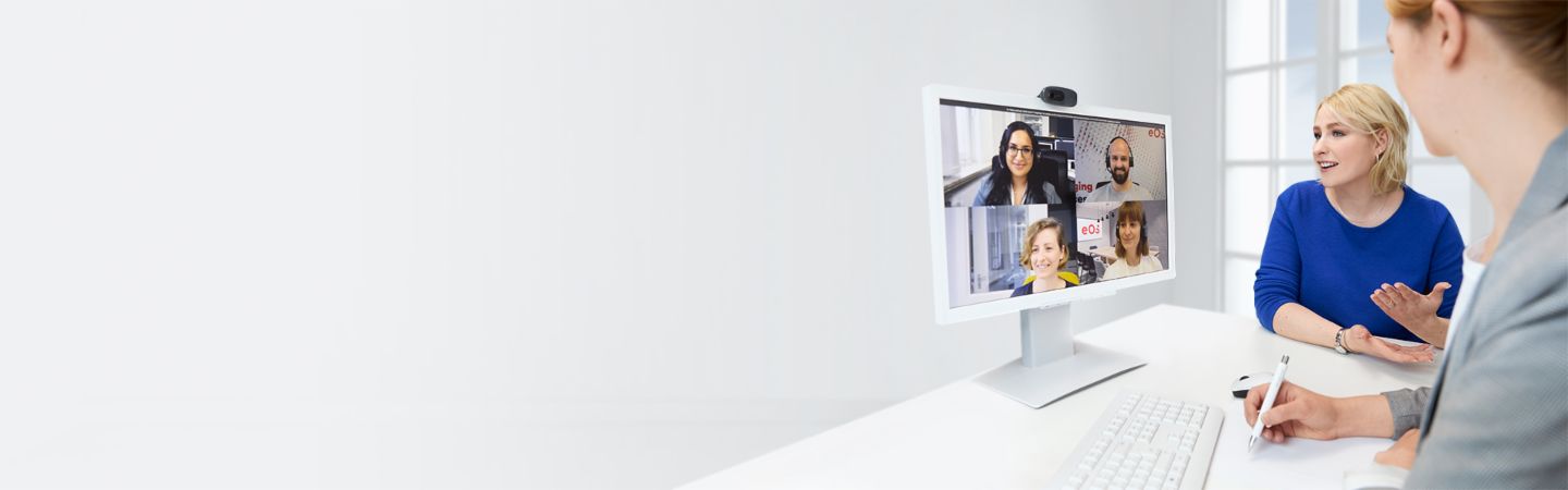 two young women sitting in front fo a monitor talking to team members in a video call