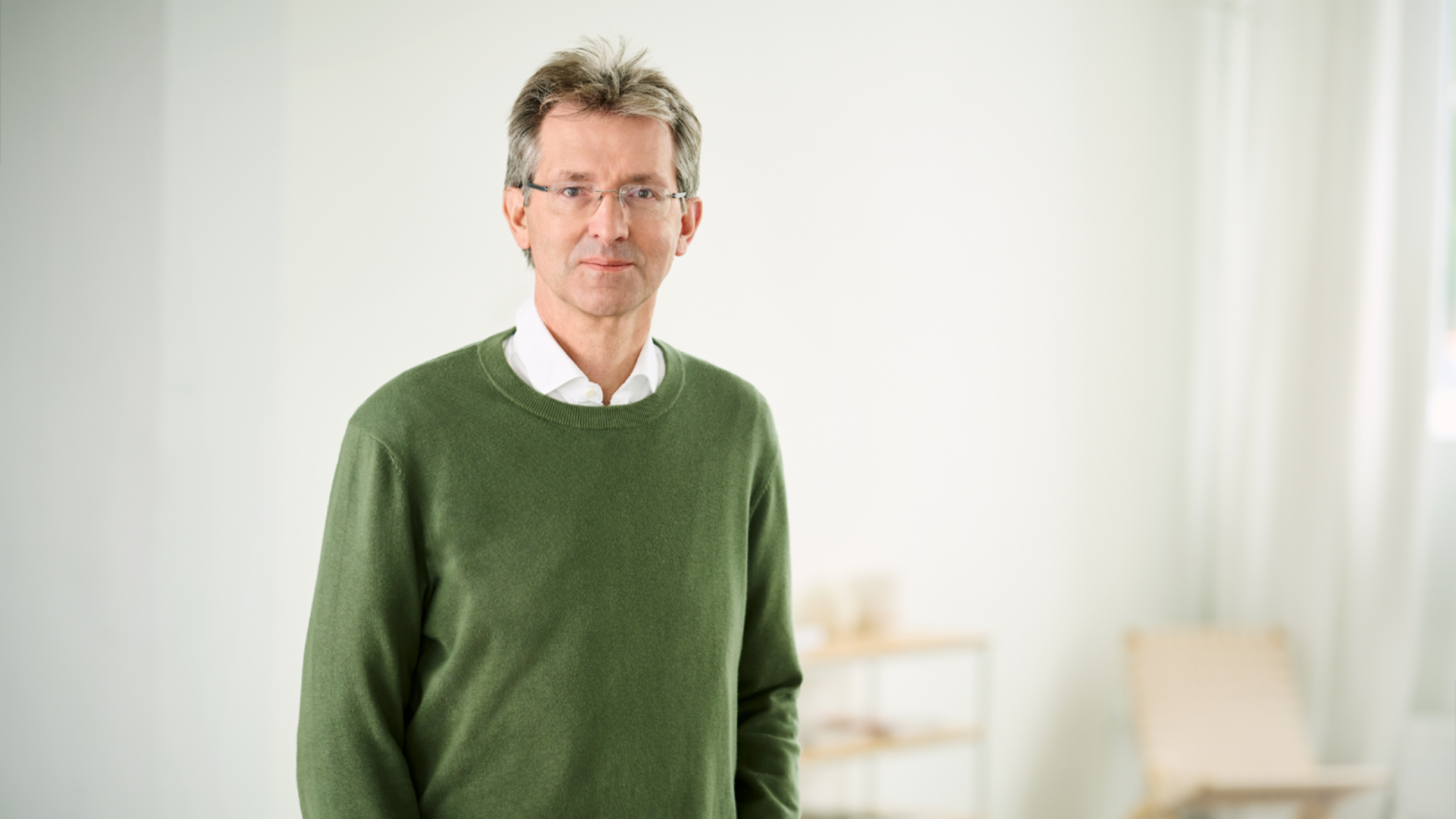 Justus Hecking-Veltman, CFO, mit einem wald-grünen Pullover und weißem Hemd, steht in einem hellen Raum.